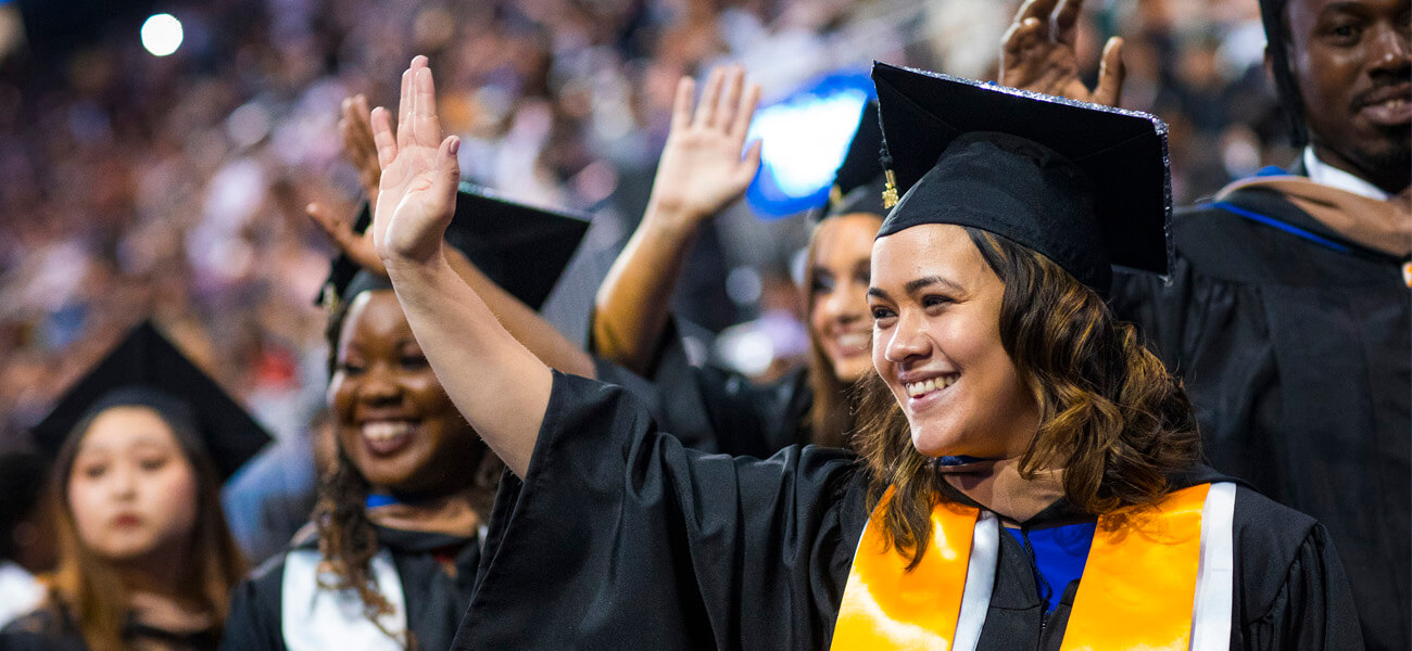 Female student in cap and down at Commencement waving