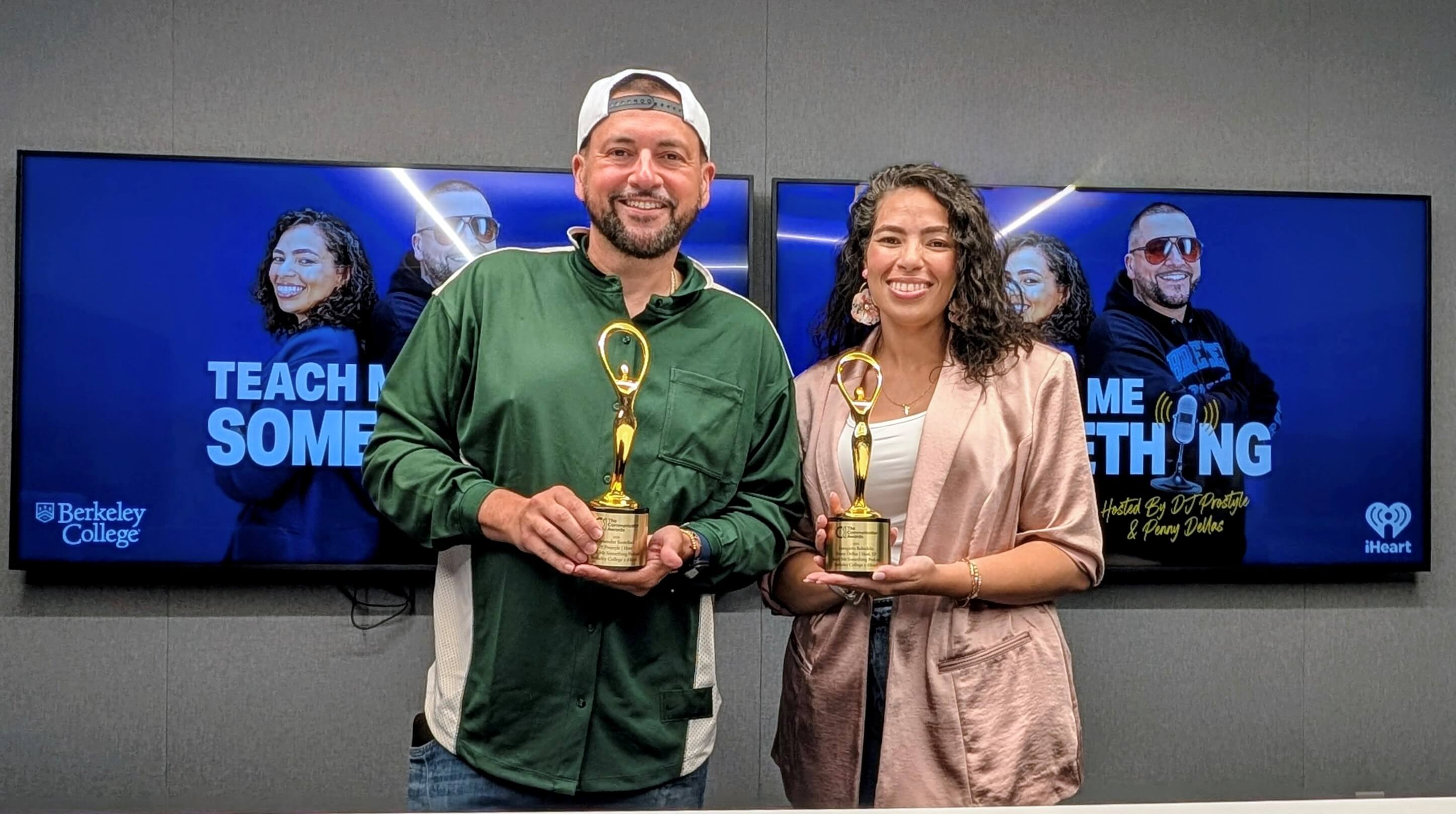 Two people smiling and holding golden awards in front of screens displaying "Teach Me Something" with Berkeley College and iHeart logos.