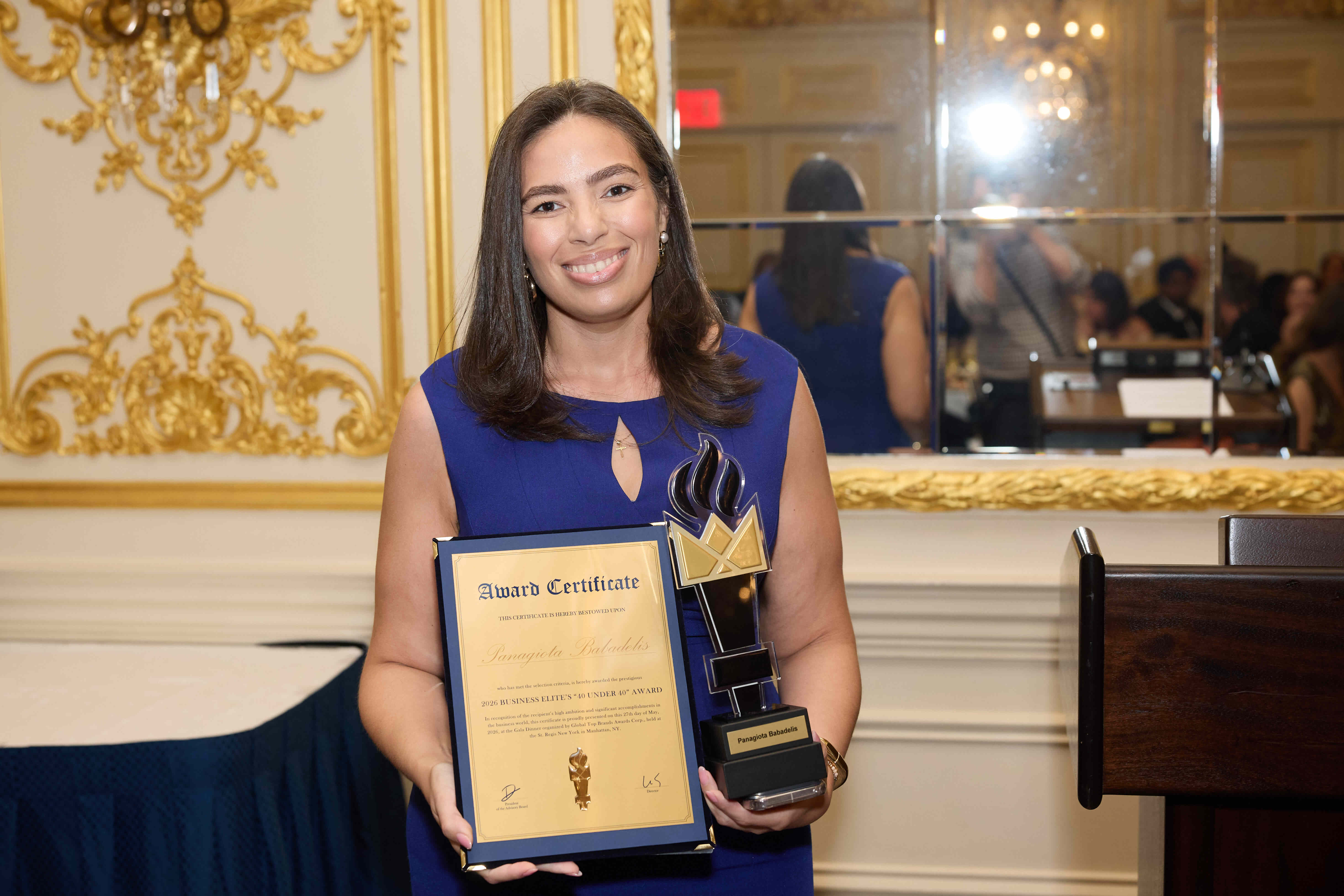 a woman in a blue dress holds a certificate in front of a mirrored backdrop