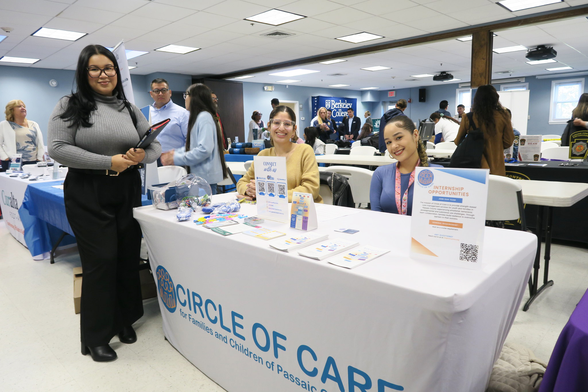 Three women at a Circle of Care internship booth with brochures and promotional items at a college event.