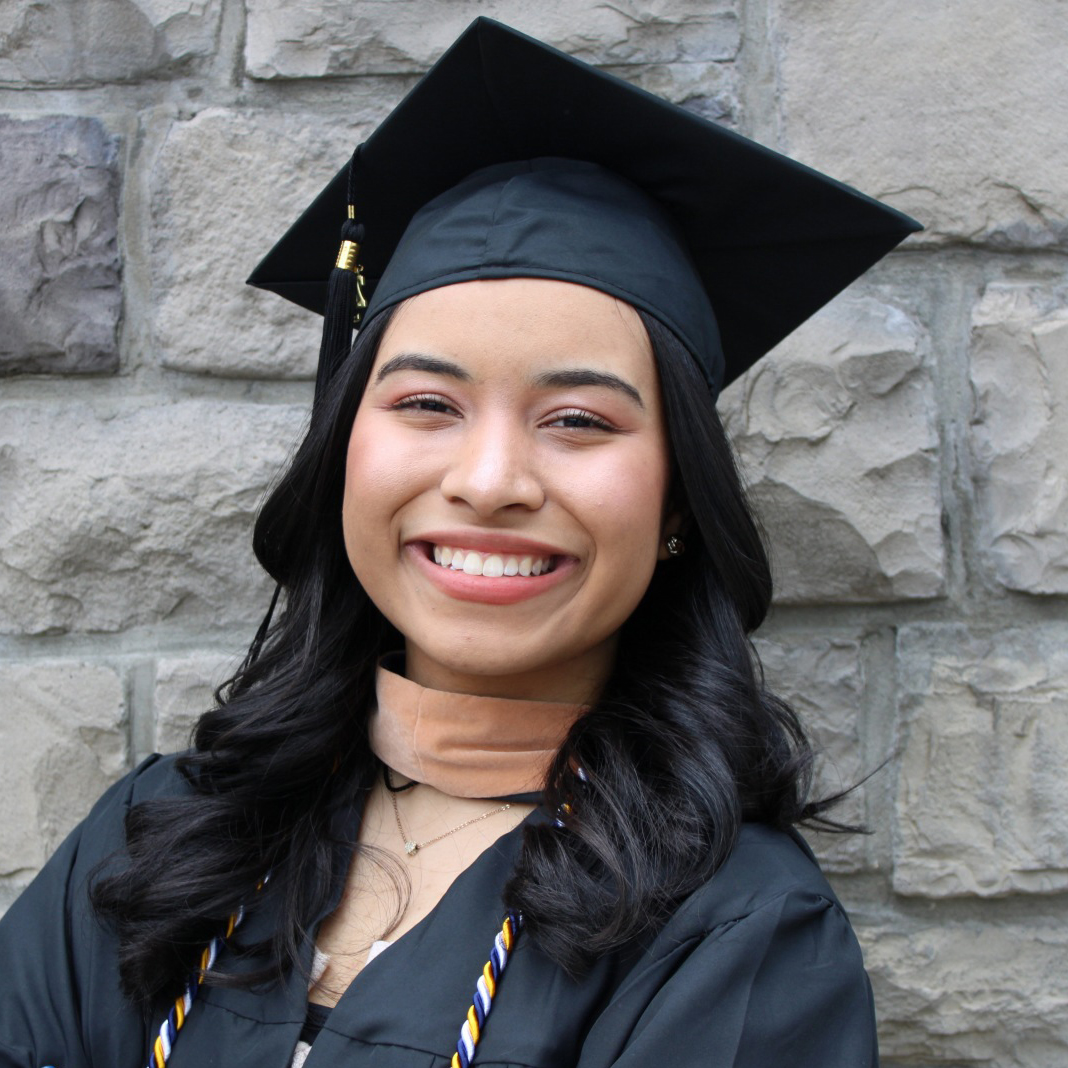 Berkeley graduate speaker Gaby Ramirez wears her cap and gown in front of a brick wall