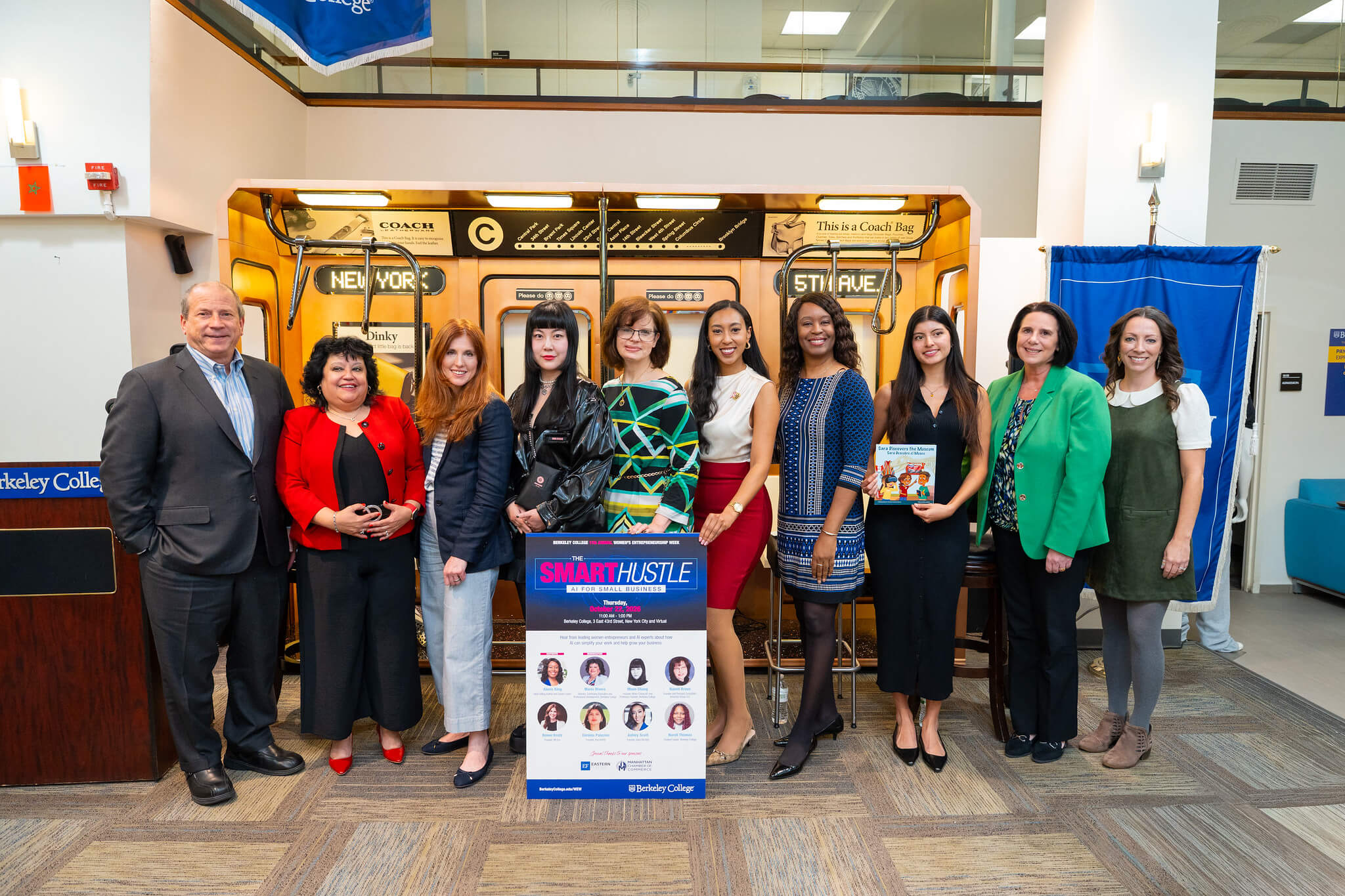 Group photo of Berkeley College’s Smart Hustle event participants posing beside a vintage Coach bag display and event poster.