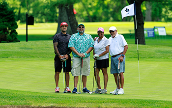 A golf foursome stands and smile at a golf course.