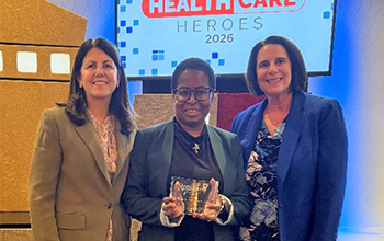 Three diverse women stand in a row and smile at the camera.
