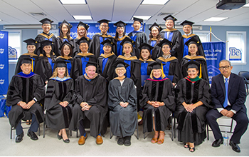 Students and faculty wearing graduation robes smiling at a graduation ceremony.