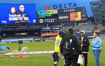 A woman and camera crew stand on a soccer field.