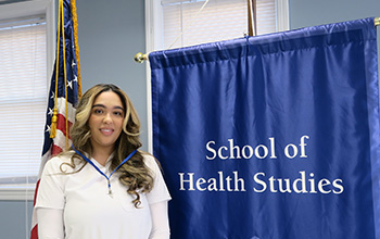 A woman in scrubs stands by two flags.