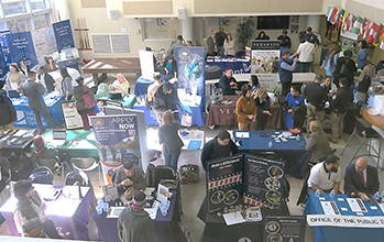 A large hall with booths and people examining booth and conversing with other people.