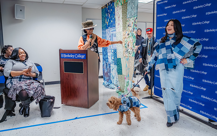 A woman at a podium points at a model and a dog in matching outfits