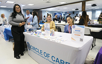 Three women at a Circle of Care internship booth with brochures and promotional items at a college event.