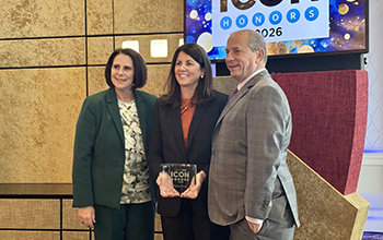 Three people posing with an ICON Honors 2026 award in front of a screen displaying the event's logo at an indoor venue.