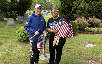 two individuals stand with american flags