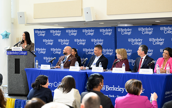 Speakers stand at a podium and sit at a table in front of a blue backdrop