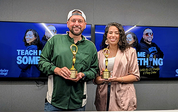 Two people smiling and holding golden awards in front of screens displaying "Teach Me Something" with Berkeley College and iHeart logos.
