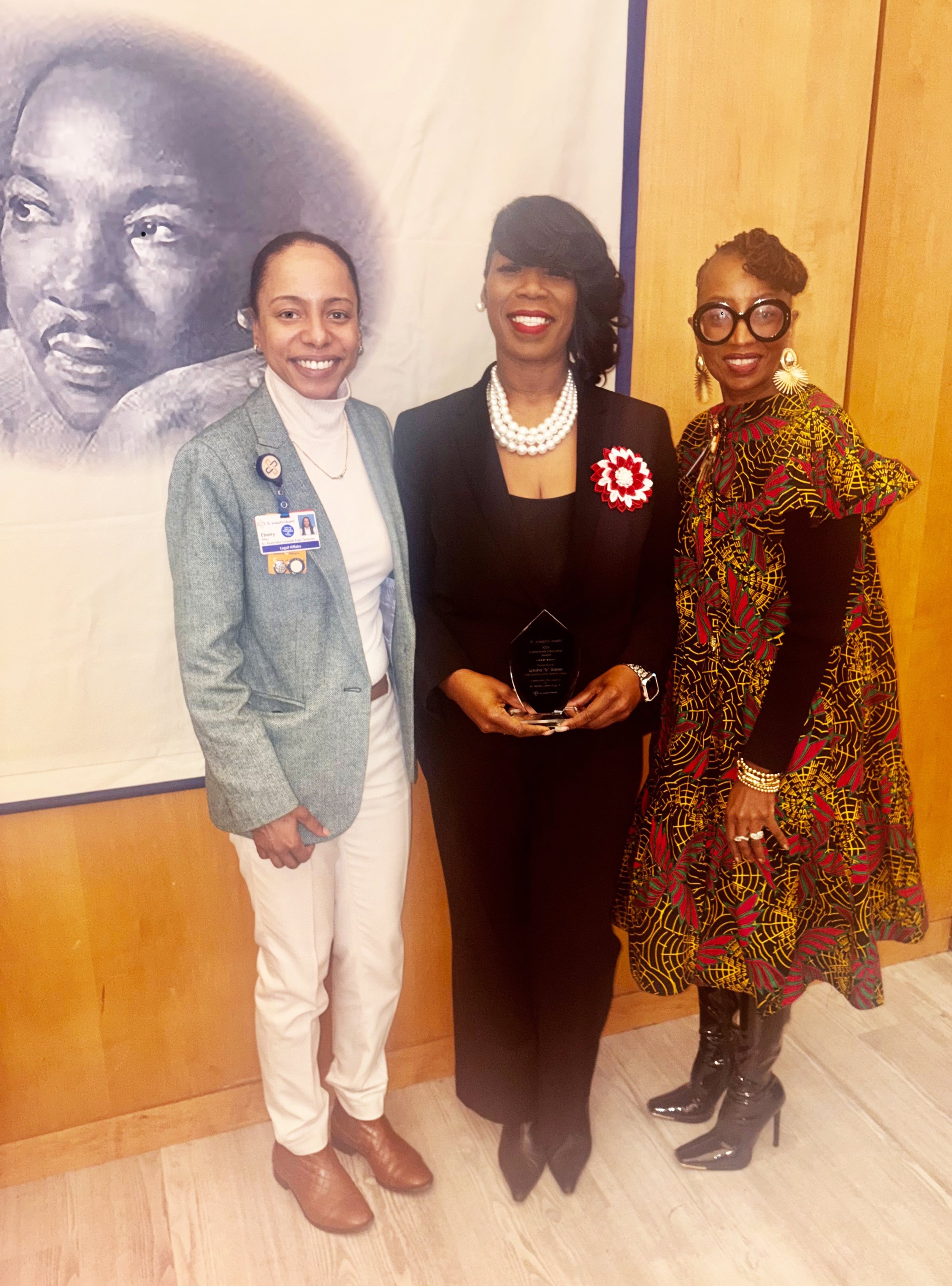 Three women smile in front of a mural of Martin Luther King Jr.