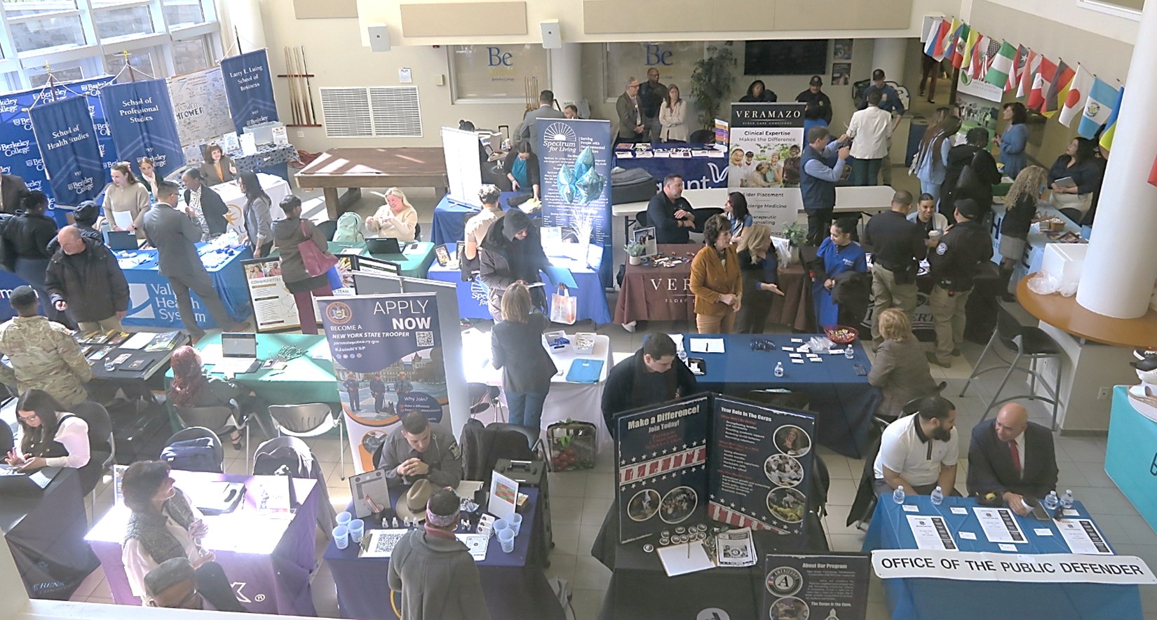 A large hall filled with display booths and people examining the booths and conversing.