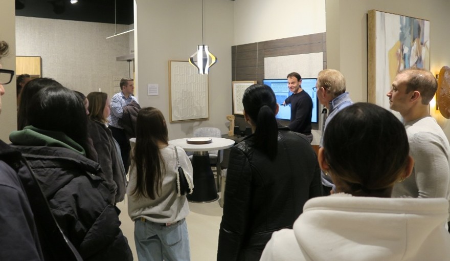 A group of people watches a man in a black sweater point to a screen in a furniture showroom.