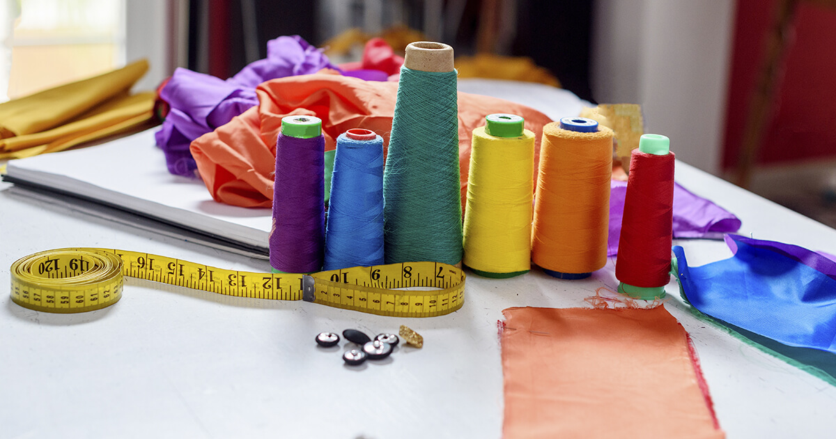Spools of colorful thread, measuring tape, and fabric swatches arranged on a table. The scene conveys a creative and vibrant sewing workspace.
