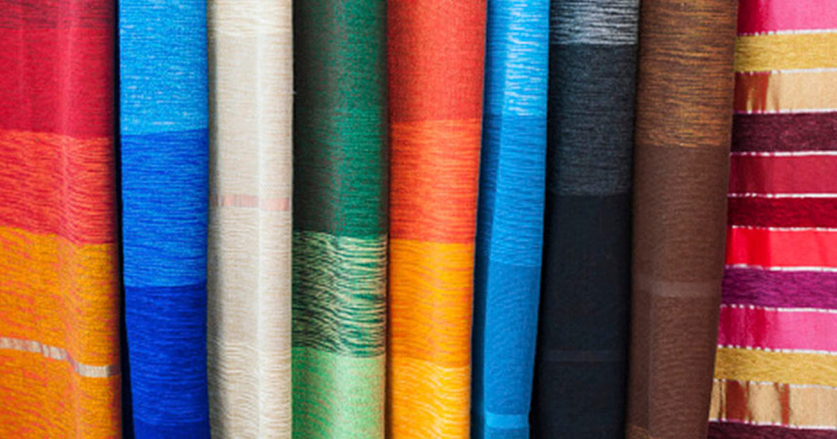 A display of vibrant textile rolls in various colors, including red, blue, green, gold, and brown, showcasing rich textures.