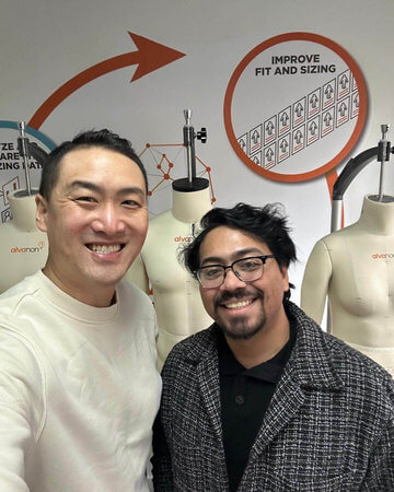 Photograph of Louis Candelario and Eric Rodriguez smiling in front of dress forms and a wall sign