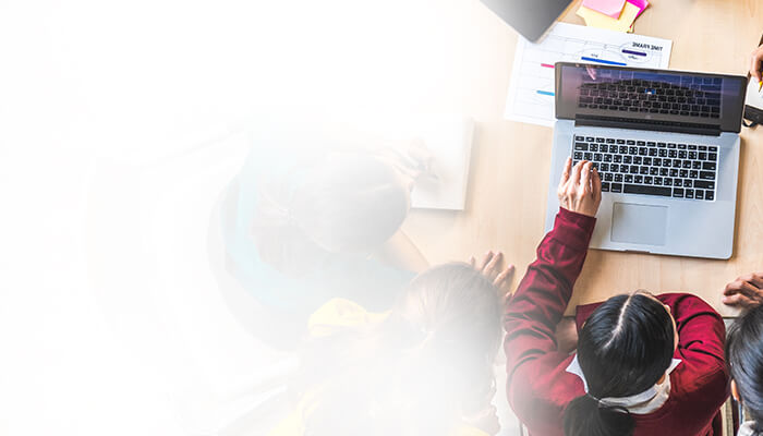 A group of individuals collaborates around a laptop at a wooden table, engaged in work or discussion.