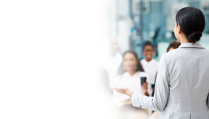 A woman in a business suit confidently presents to an audience, showcasing her professional expertise and communication skills