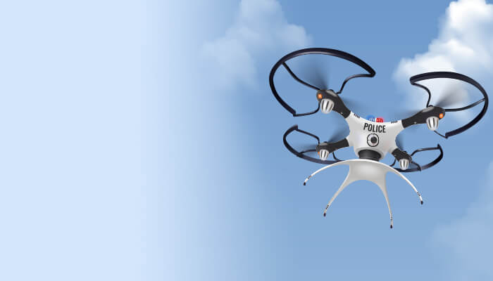 A police drone hovers against a blue sky with fluffy clouds. The drone's sleek design and visible camera suggest surveillance capabilities.
