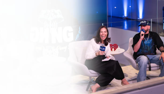 A female and male host speaking into iHeartRadio microphones during a live panel discussion on a modern stage set