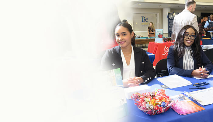 Two women smile at a colorful information table with brochures and candy at a busy professional event, creating a welcoming atmosphere