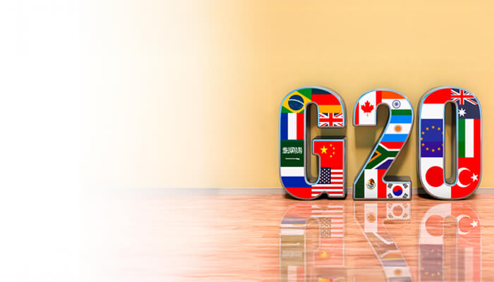 3D letters "G20" decorated with member country flags stand against a light yellow wall. The polished floor reflects the vibrant colors, conveying unity.