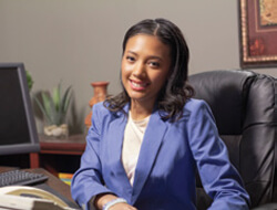 A woman in a business suit seated at a desk, focused on her work with a laptop and documents in front of her