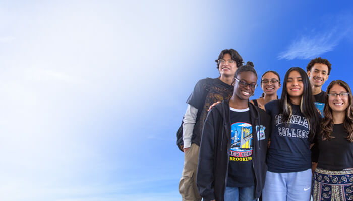 A group of eight individuals wearing matching black T-shirts stands together, smiling against a clear blue sky backdrop.