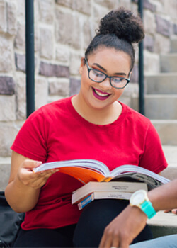 Female student looking at text books sitting on outside step