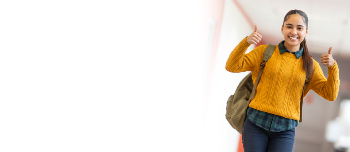 A person in a yellow sweater gives a thumbs-up while wearing a backpack in a brightly lit hallway