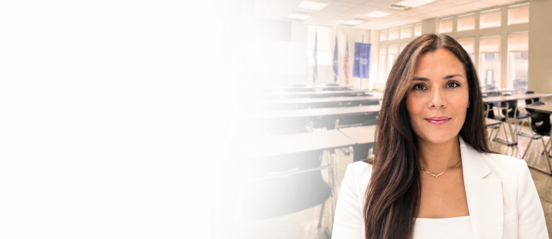 Image of Michelle Gomez standing confidently in a bright classroom, wearing a blue blazer and white shirt, conveying professionalism.