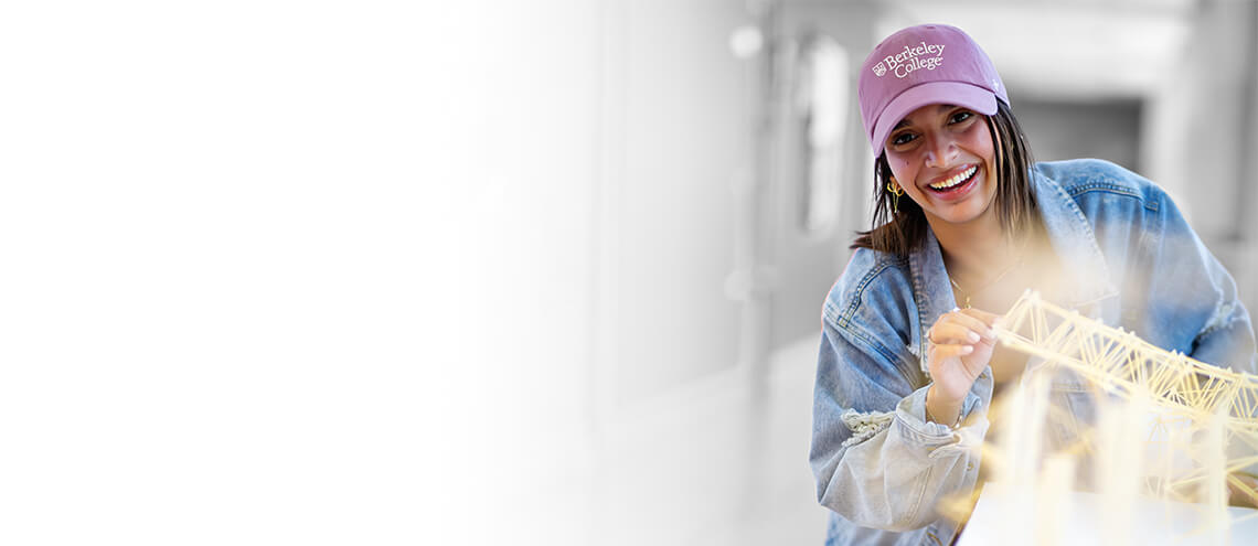 A woman wearing a pink hat smiles brightly while holding a piece of paper in her hands.