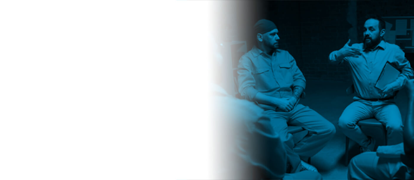 A group of individuals in uniform sit in a circle, engaged in conversation in a dimly lit room with a blue hue.