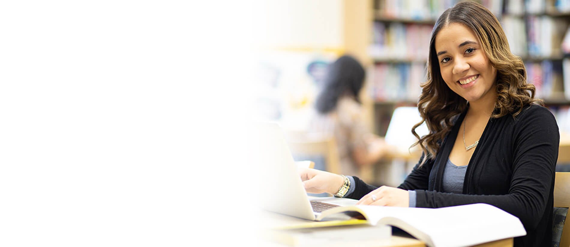 A cheerful woman at a table uses her laptop, radiating positivity and focus in her workspace