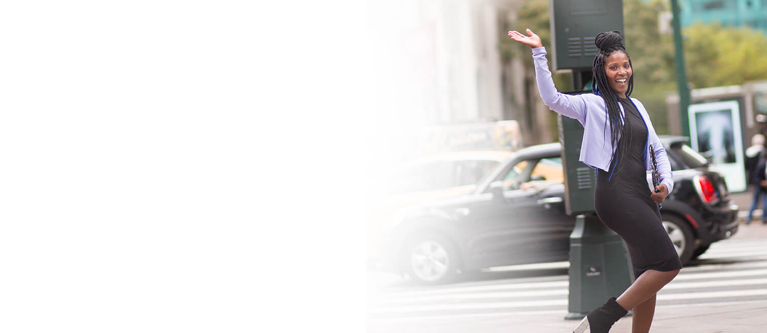 A woman wearing a black dress and high heels strides across the street, embodying elegance and sophistication