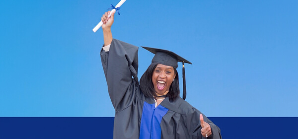 Joyful graduate in a black cap and gown raises her diploma overhead and gives a thumbs-up against a blue background, celebrating success