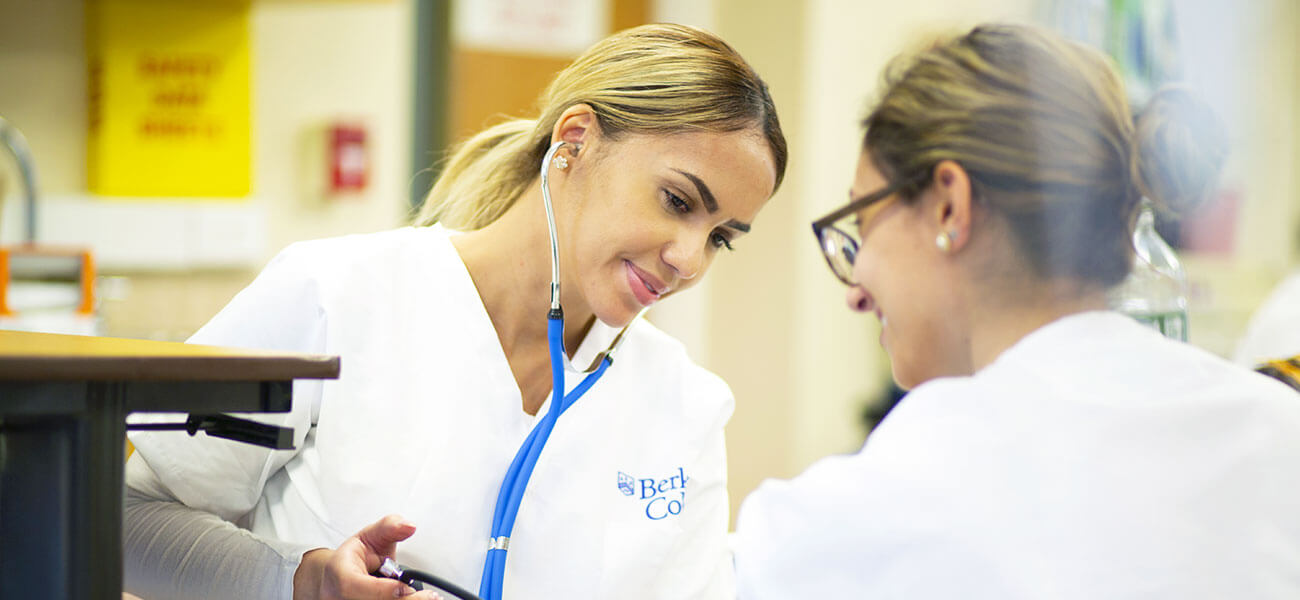 Two female nursing students smiling and taking blood pressure while listening to a stethoscope