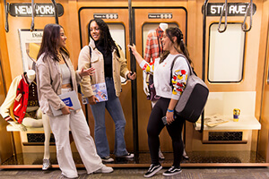 Three stylishly dressed women confidently smiling in front of a subway train