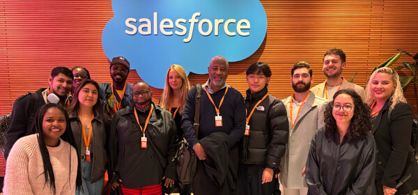 Group of individuals posing together in front of a Salesforce logo, showcasing a diverse gathering in a professional setting.