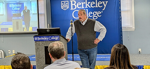 A man stands at a podium, delivering a presentation to an audience at a professional conference