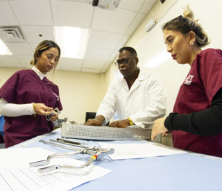 2 female students and professor looking at surgical tools.  mobile image