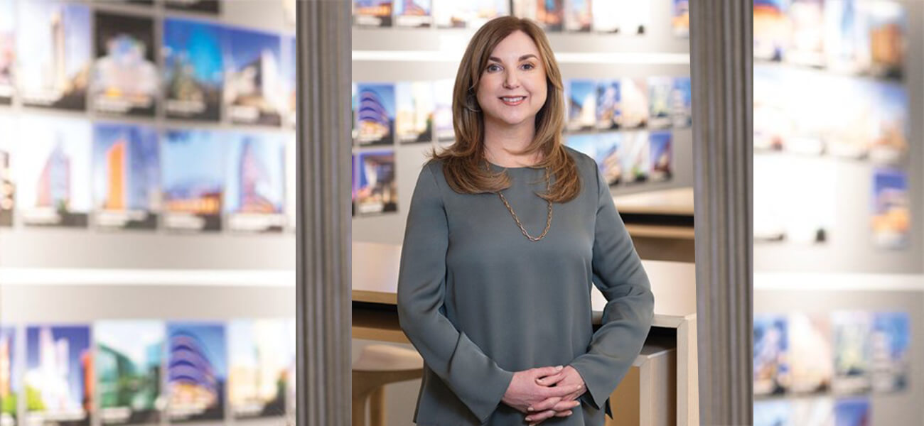 A woman stands thoughtfully in front of a collage of photographs displayed on a wall