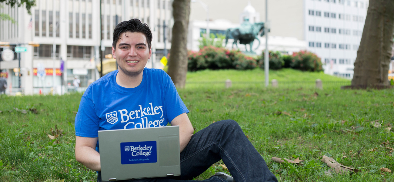 Student wearing a Berkeley College shirt working on laptop outside
