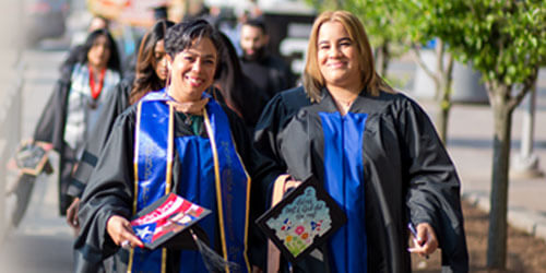 Two women in graduation gowns joyfully walking down the street, celebrating their academic achievements together