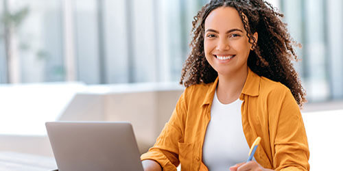 A woman seated at a table, focused on her laptop, engaged in work or study