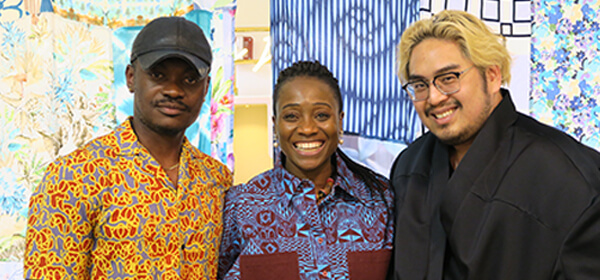 Three designers-in-residence smile and pose for a photo in front of a fabric backdrop